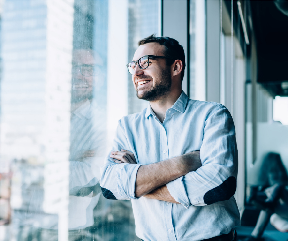 Smiling man with his arms crossed looking out of office window